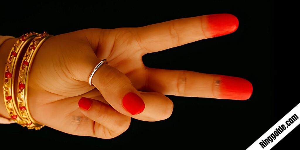Hand making peace sign wearing gold bangles and curved silver ring with vibrant red nail polish