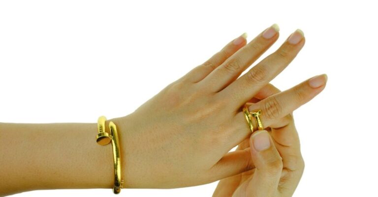 A woman's hand elegantly holds a gold bracelet, showcasing its shine and craftsmanship.