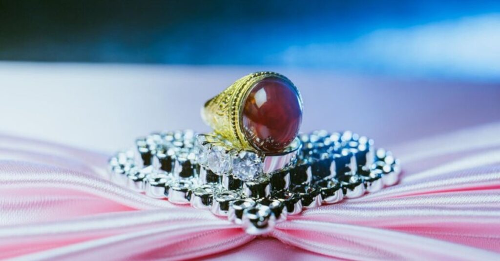 A ring featuring a red stone, elegantly placed on a soft pink cloth.